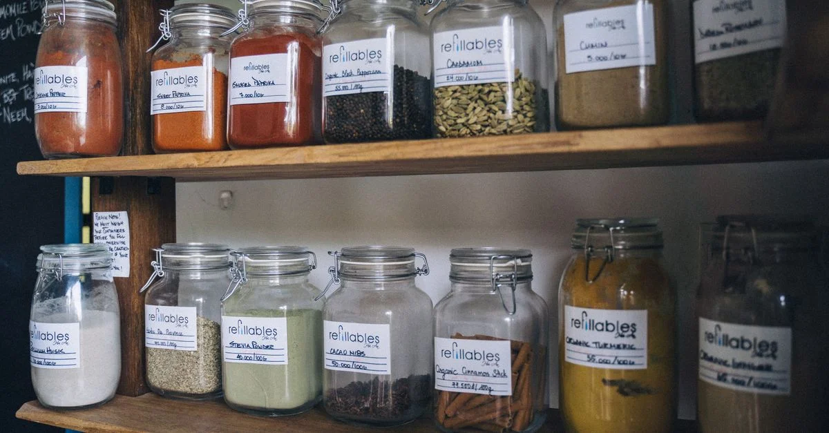 Des bocaux en verre remplis d'épices et d'étiquettes sur une étagère en bois pour un stockage écologique.