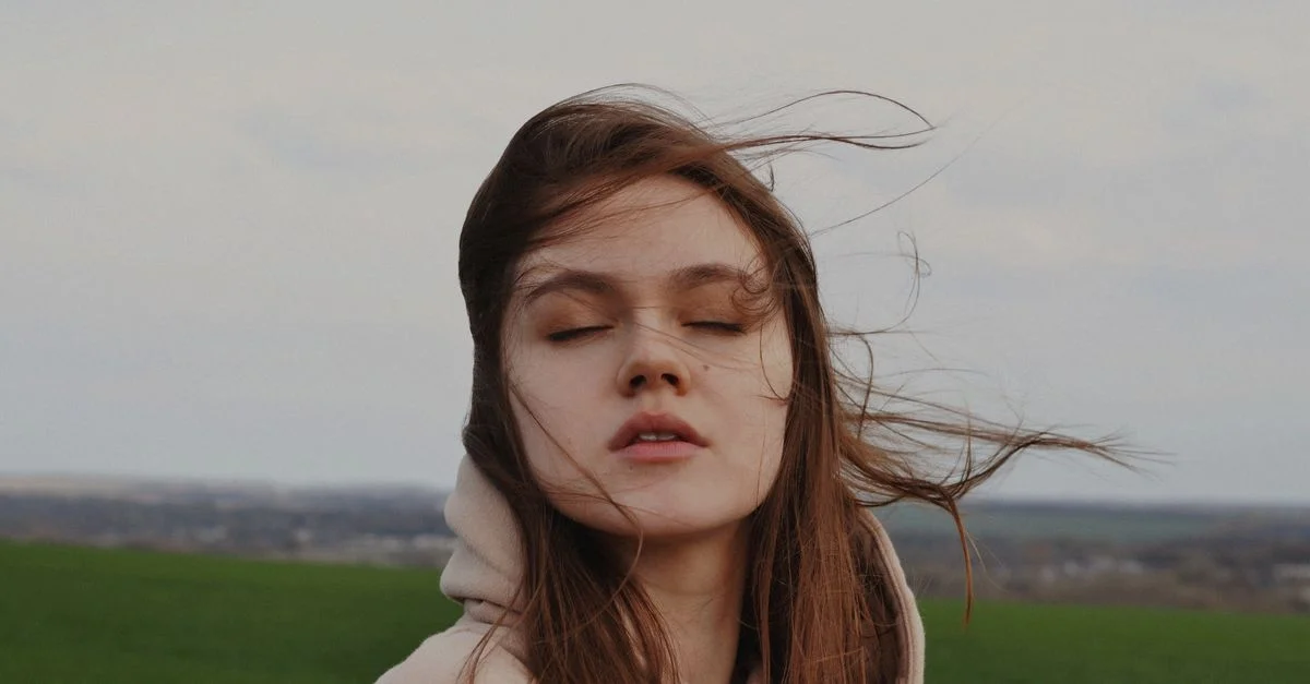 Jeune femme les yeux fermés profitant du vent dans un champ ouvert. Un moment de paix et de sérénité.