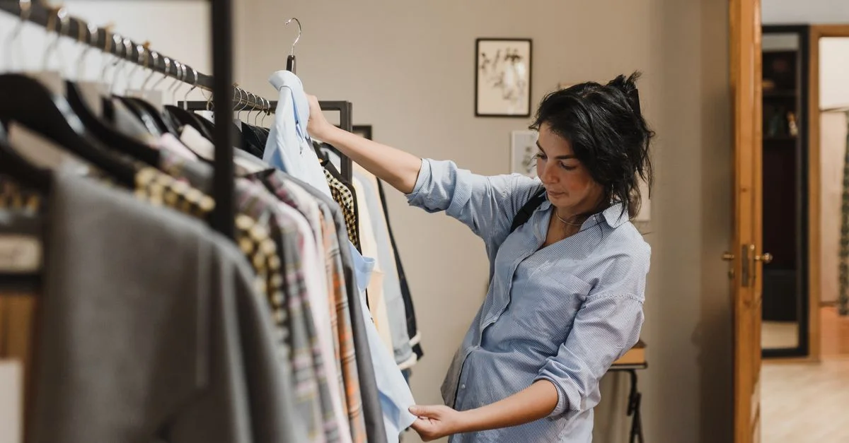 Une femme examine des vêtements sur un portant dans une boutique élégante, en considérant ses options d'achat.