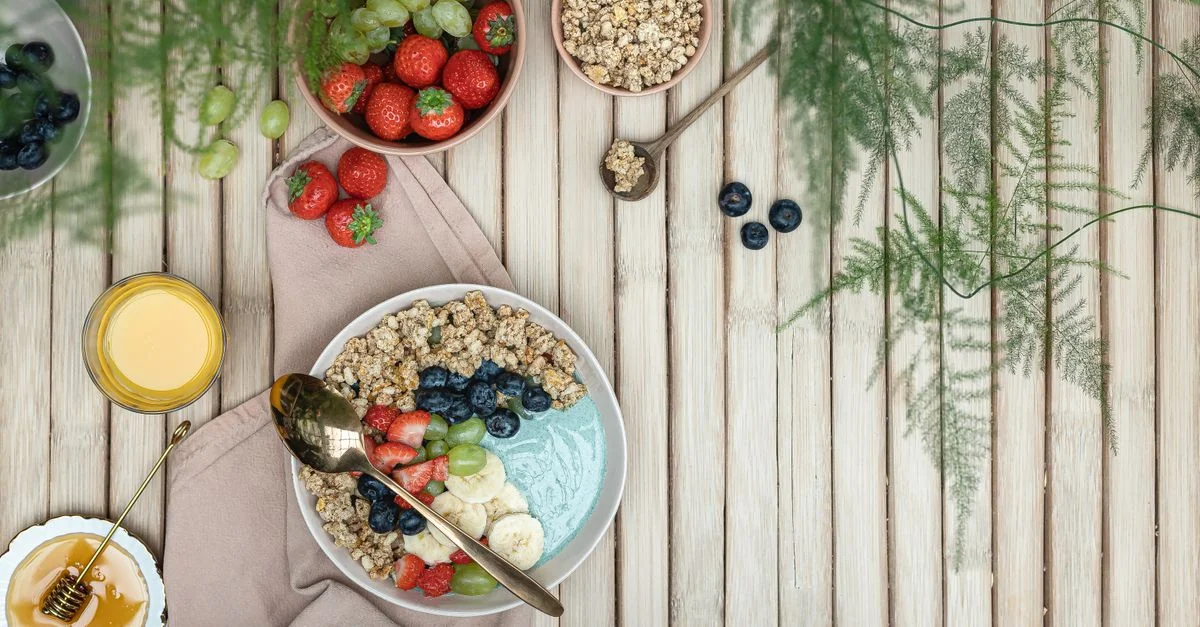 Un bol de petit déjeuner coloré avec des fruits frais, du granola et du miel sur une table en bois rustique.