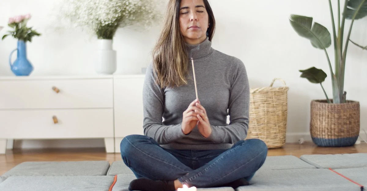 Une femme pratiquant la méditation de pleine conscience à l'intérieur, tenant de l'encens.