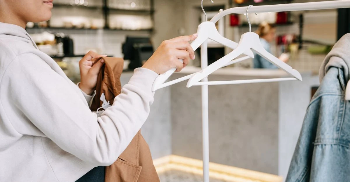 Une femme parcourant et choisissant des vêtements dans une boutique moderne au décor minimaliste.