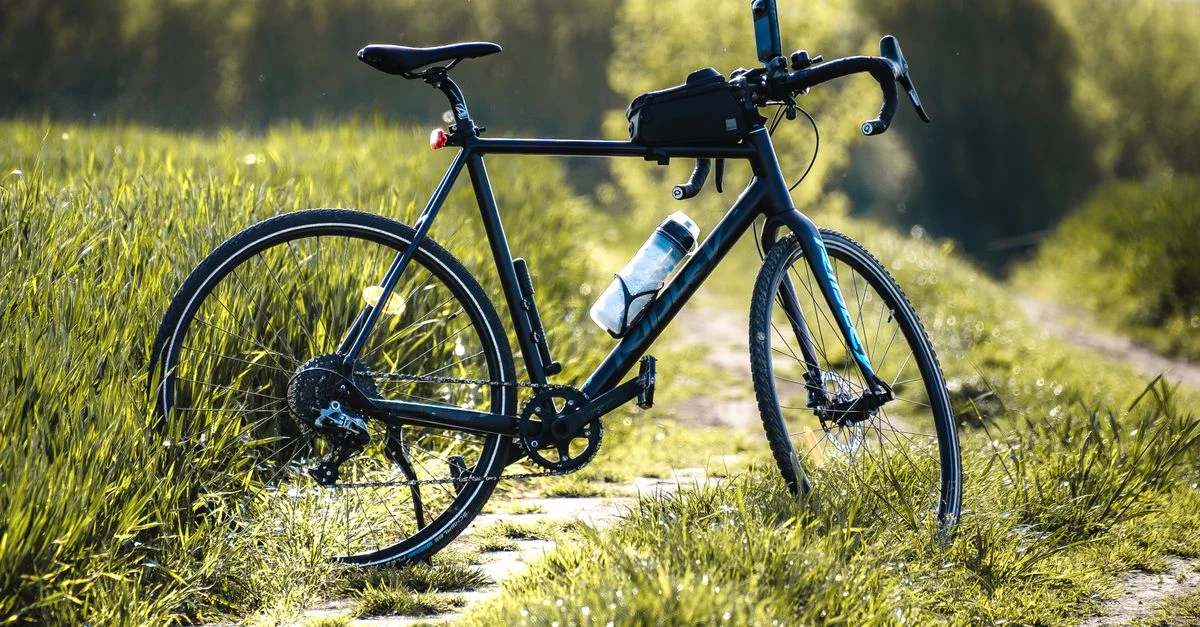 Un vélo repose sur un chemin herbeux sous la lumière vive du jour.