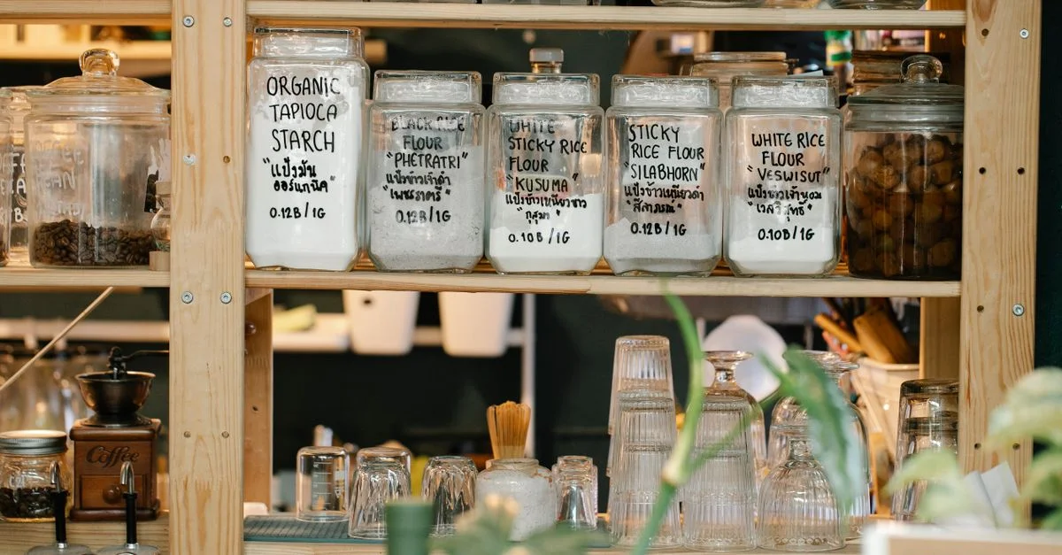 Une variété de bocaux de farine exposés sur une étagère en bois de garde-manger avec des plantes.
